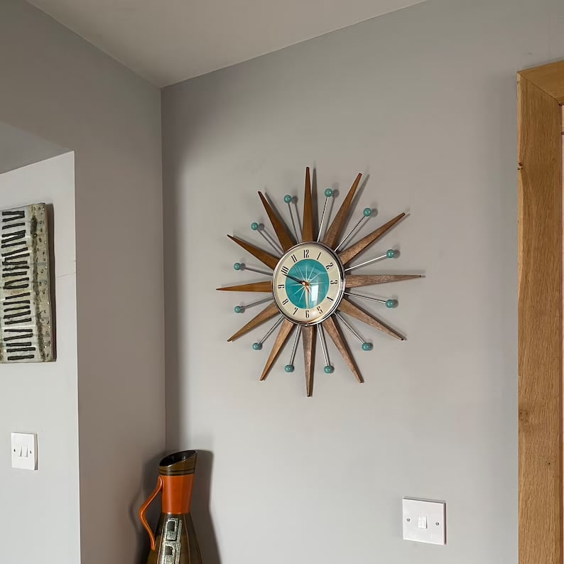 Horloge étoile en situation dans un coin de salon gris, avec un vase orange rétro et un cadre décoratif au mur. 6