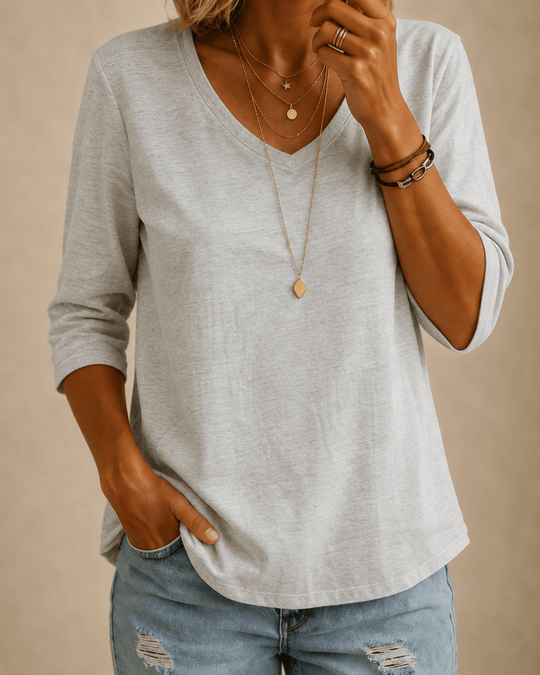Femme portant le haut gris chiné à col en V avec un jean déchiré et des colliers fins 1