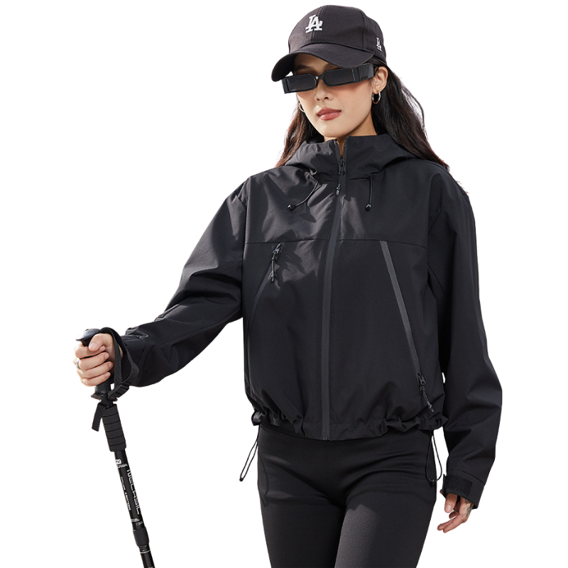 Veste courte noire à capuche portée avec casquette et lunettes, bâton de marche à la main, cordons d'ourlet serrés. 14