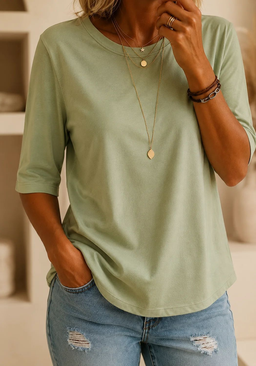 T-shirt vert sauge à demi-manches porté avec un jean troué, dans un intérieur clair avec étagères beiges. 11