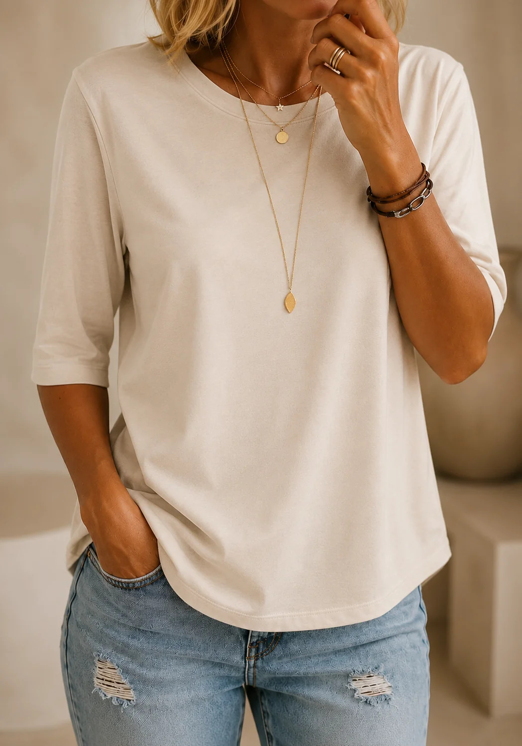 T-shirt crème à demi-manches porté avec un jean clair et des colliers dorés, dans un intérieur aux tons beiges. 10