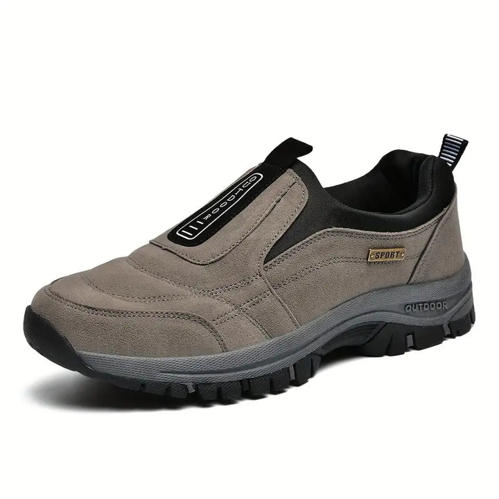 Mocassin sans lacets en suédine gris-taupe, vu de trois quarts, avec semelle crantée épaisse et talon à petite boucle de tirage. 1