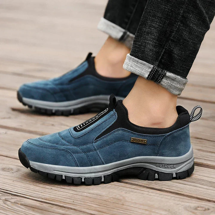 Chaussures bleues portées avec un jean noir retroussé sur un plancher en bois, vues de côté pour montrer la semelle crantée. 5