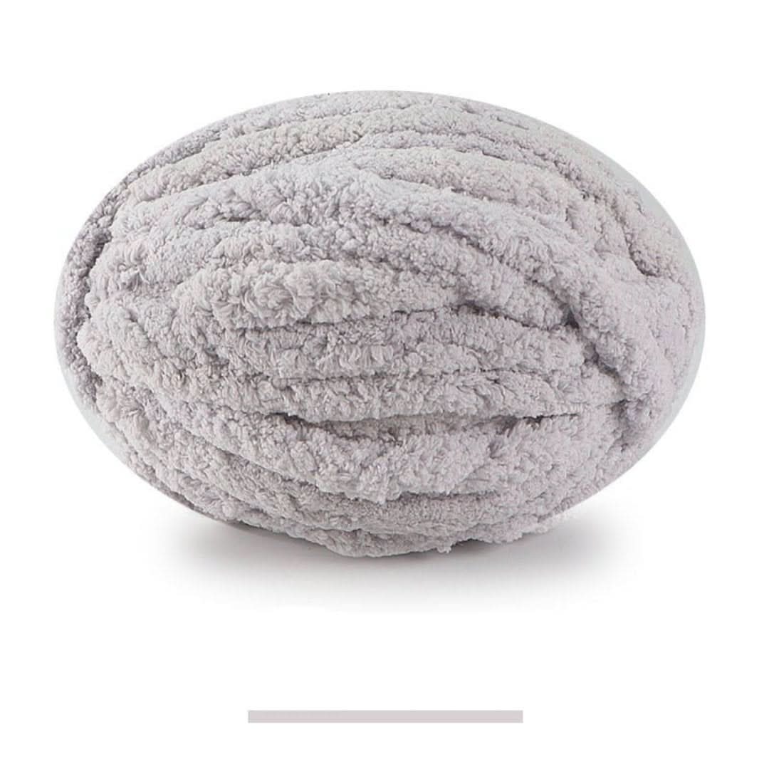 Pelote ovale de fil épais et moelleux gris clair, sur fond blanc, avec un échantillon de la teinte en dessous. 18
