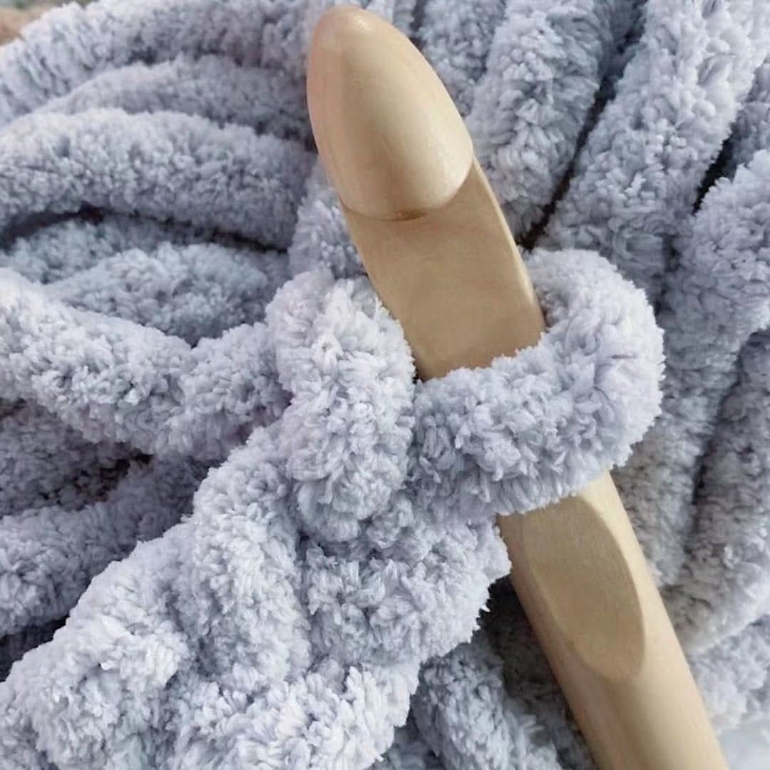 Gros plan sur un crochet en bois très épais accroché à une maille douce et duveteuse gris clair. 3