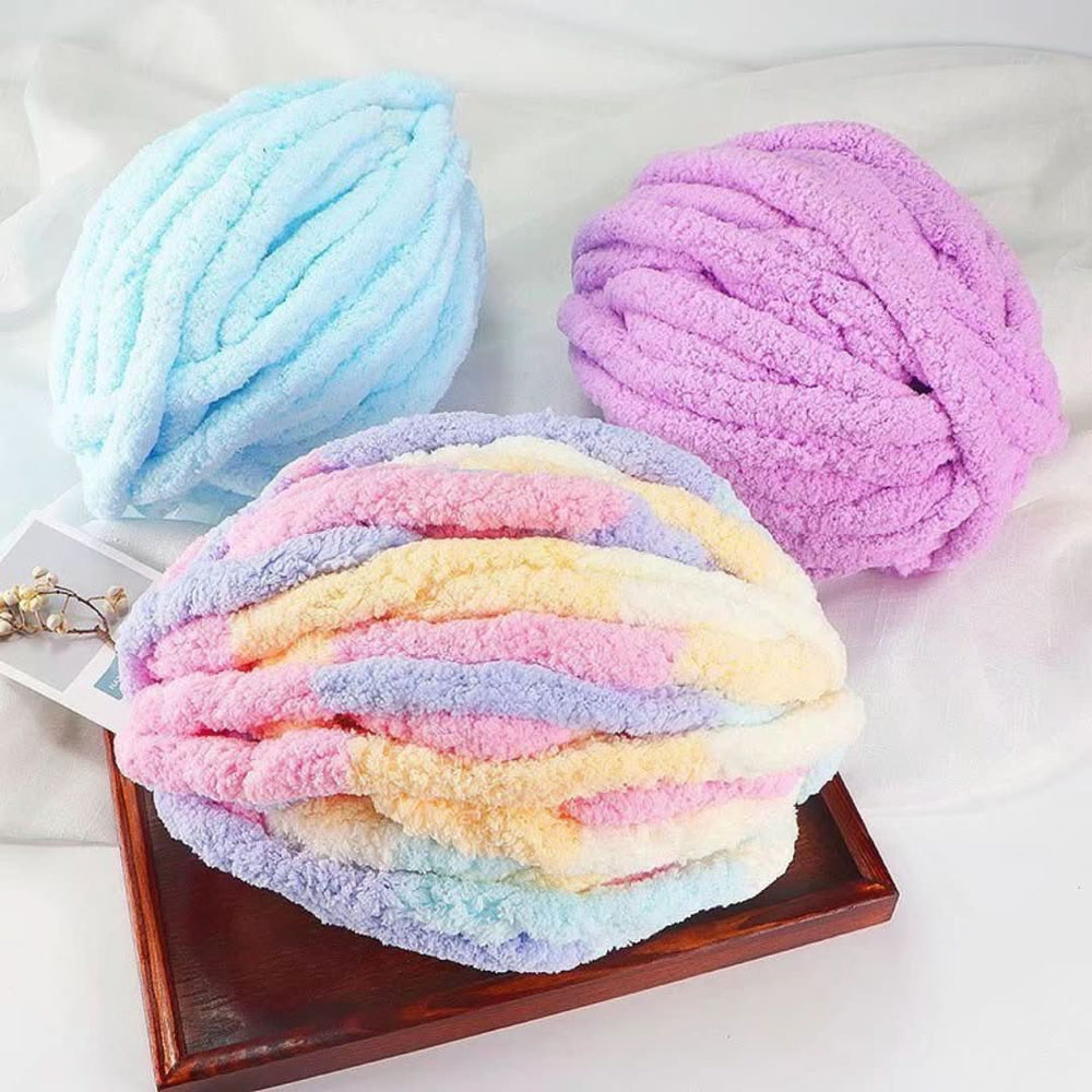 Trois pelotes de fil moelleux en grosse torsade : une bleu ciel, une violette et une multicolore pastel, posées sur un plateau en bois. 2