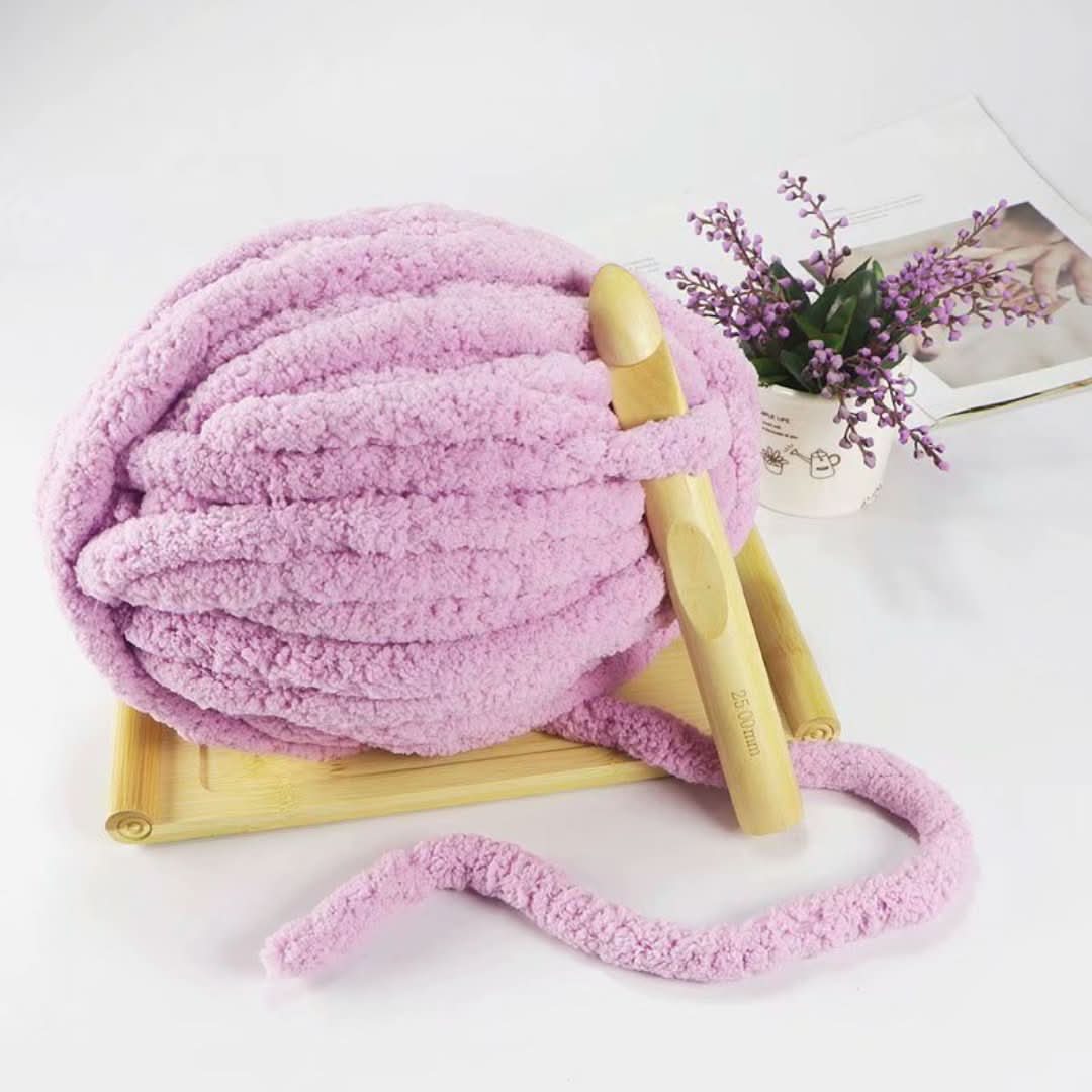 Pelote rose clair de fil duveteux avec un gros crochet en bois planté dedans, sur un support en bambou et près d'un petit bouquet. 4