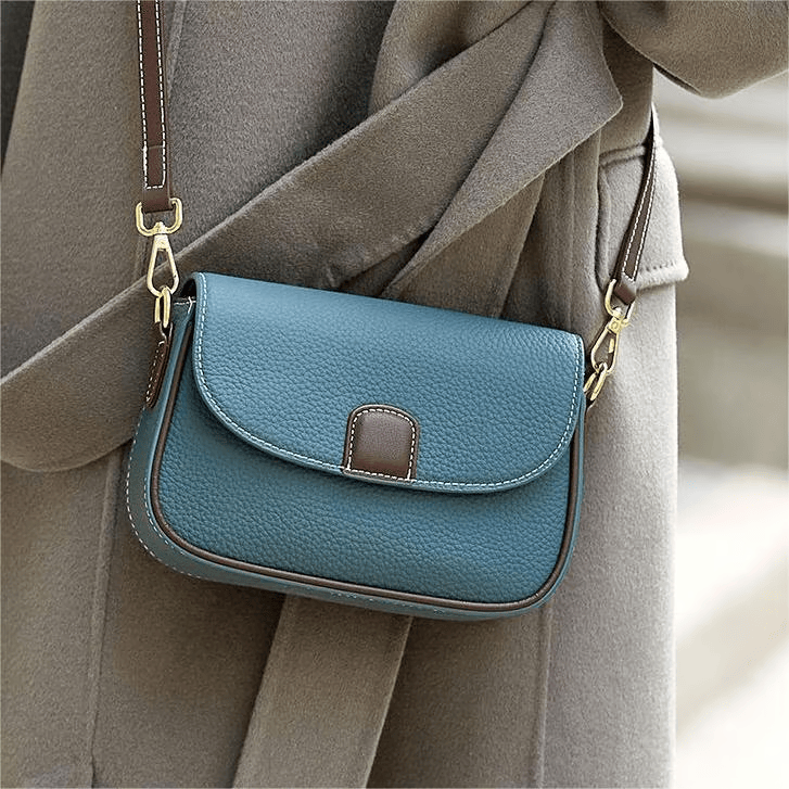 Sac bleu pétrole porté en bandoulière sur un manteau gris, avec mousquetons dorés et liseré brun 4