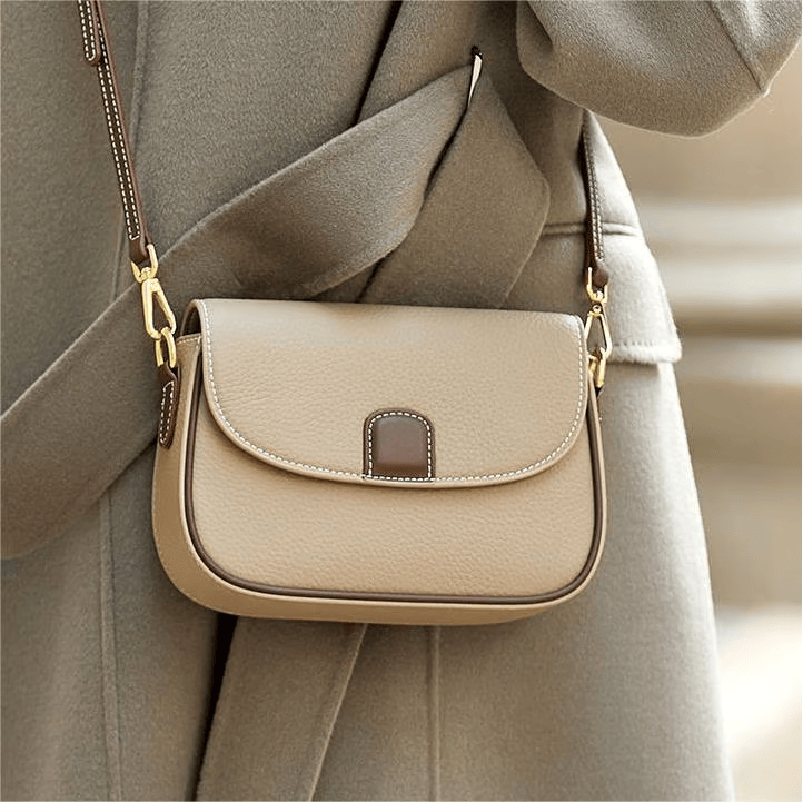Sac beige porté en bandoulière sur un manteau gris-vert, rabat arrondi et patte de fermeture brune 3