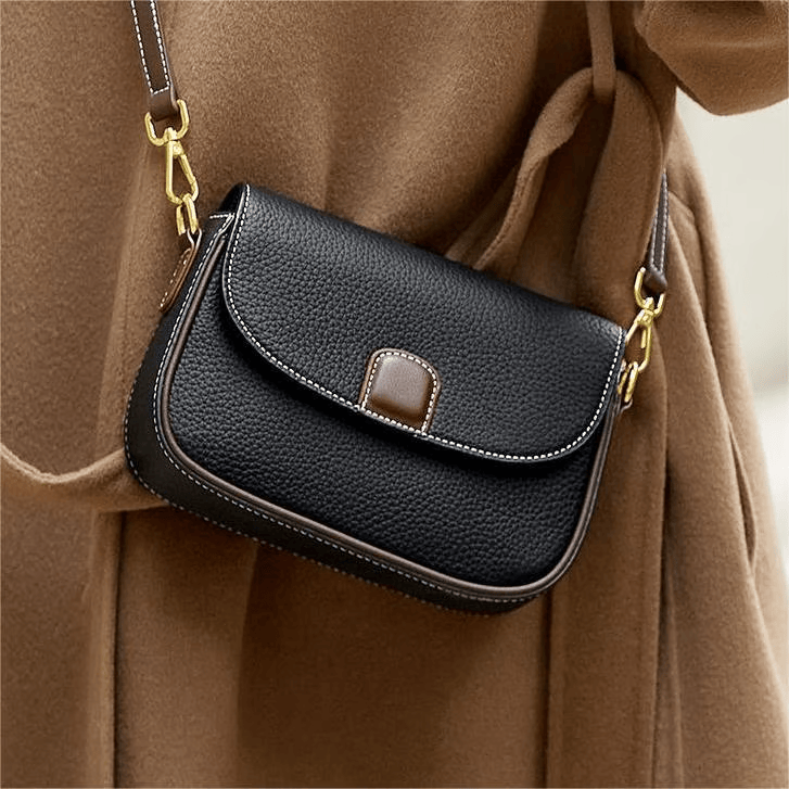 Sac noir en cuir grainé porté en bandoulière sur un manteau camel, surpiqûres blanches et fermoir brun 1