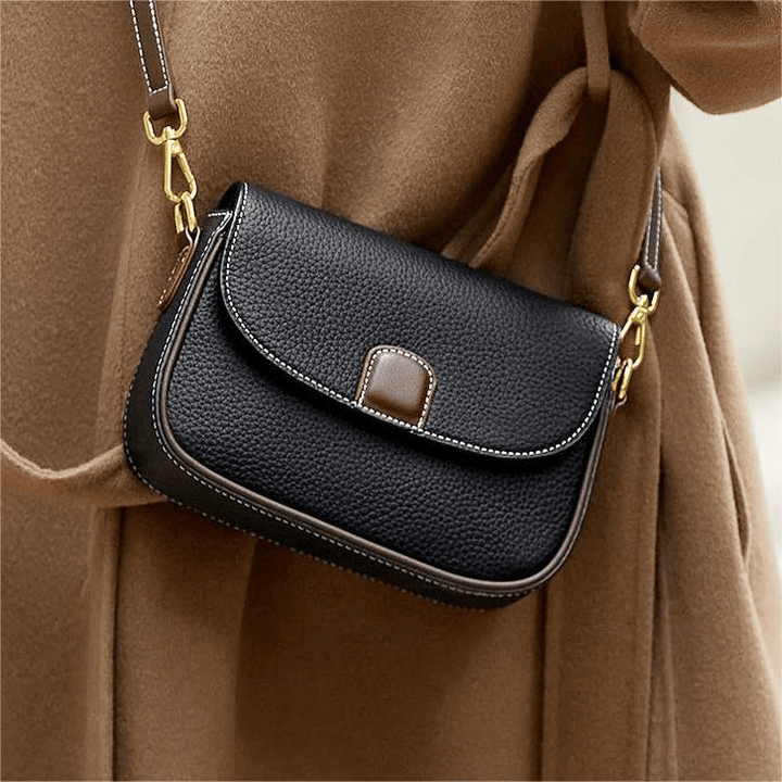 Sac noir en cuir grainé porté en bandoulière sur un manteau camel, surpiqûres blanches et fermoir brun 1