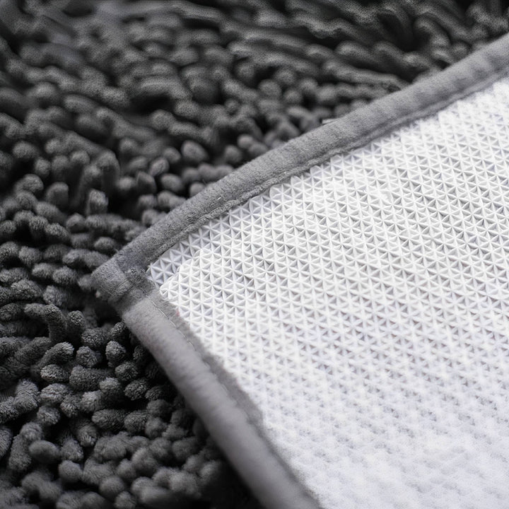 Détail du dos blanc antidérapant alvéolé et du bord cousu du tapis, rabattu sur les mèches de chenille sombres. 8