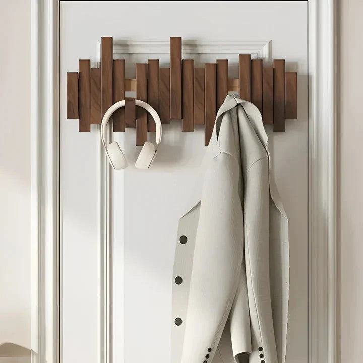 Portemanteau en bois foncé sur une porte blanche, avec un casque audio et une veste claire accrochés 2