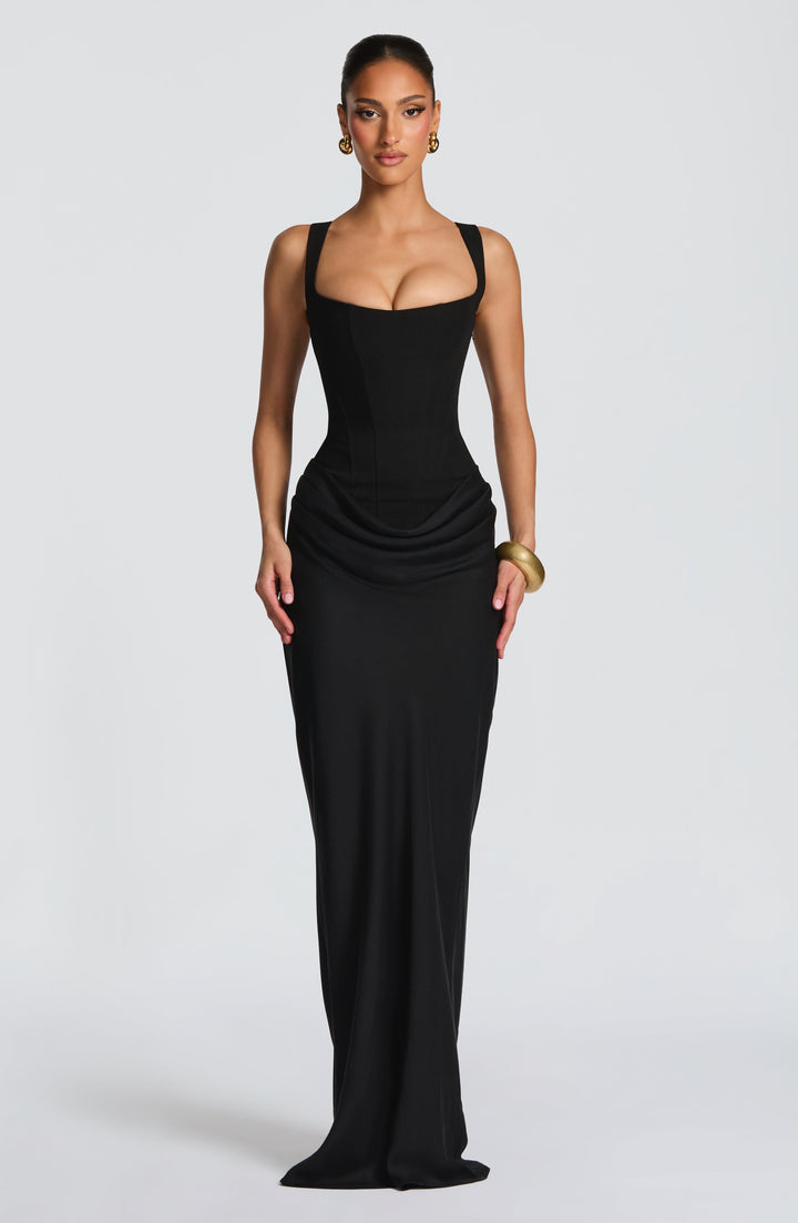 Robe longue noire portée de face, corset structuré, décolleté carré, drapé aux hanches et jupe ajustée. 12
