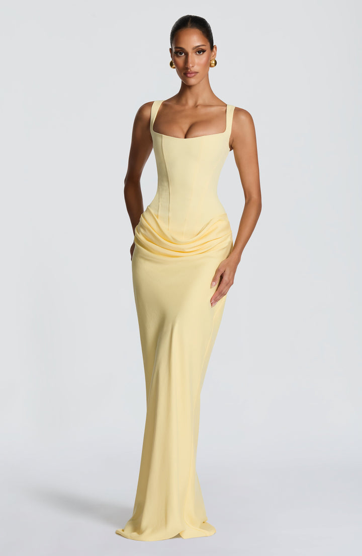 Robe jaune pâle portée en trois quarts, mettant en valeur le corset ajusté, le drapé aux hanches et la jupe fluide. 34