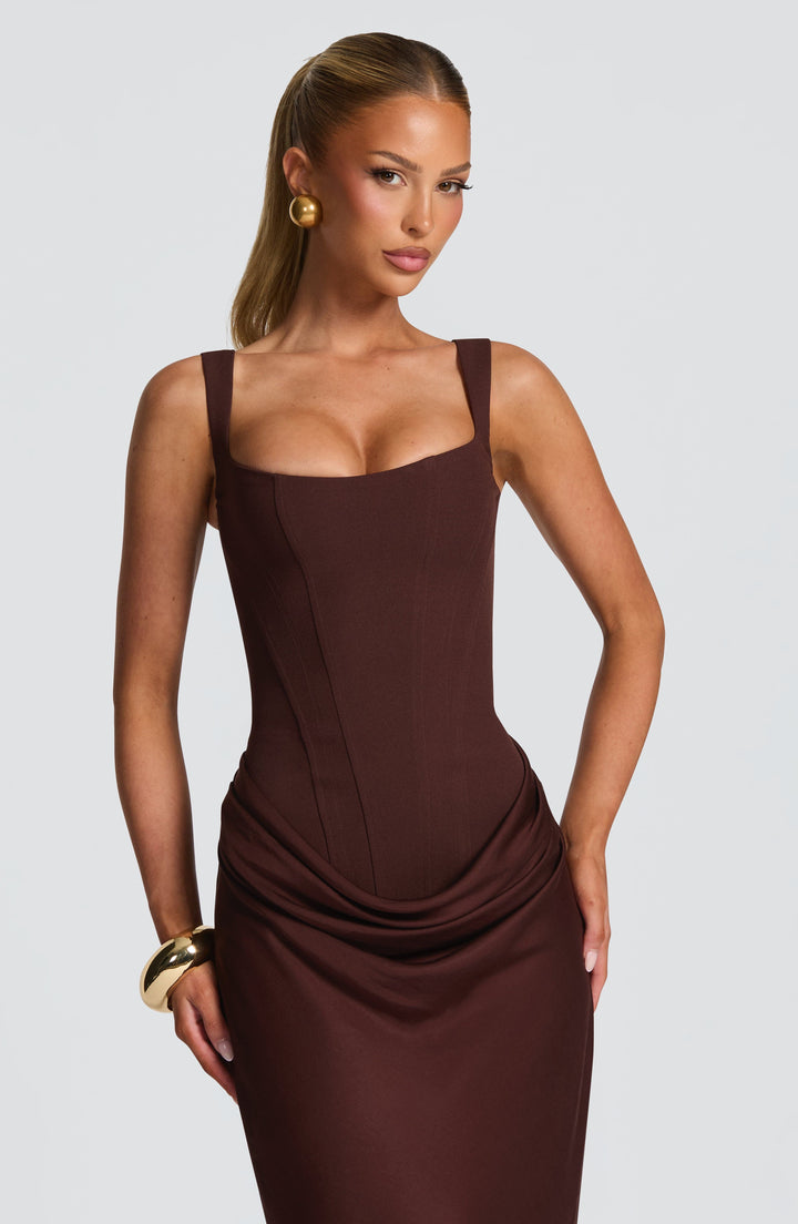 Gros plan sur le buste corseté marron, avec ses coutures verticales, ses larges bretelles et le drapé à la taille. 4