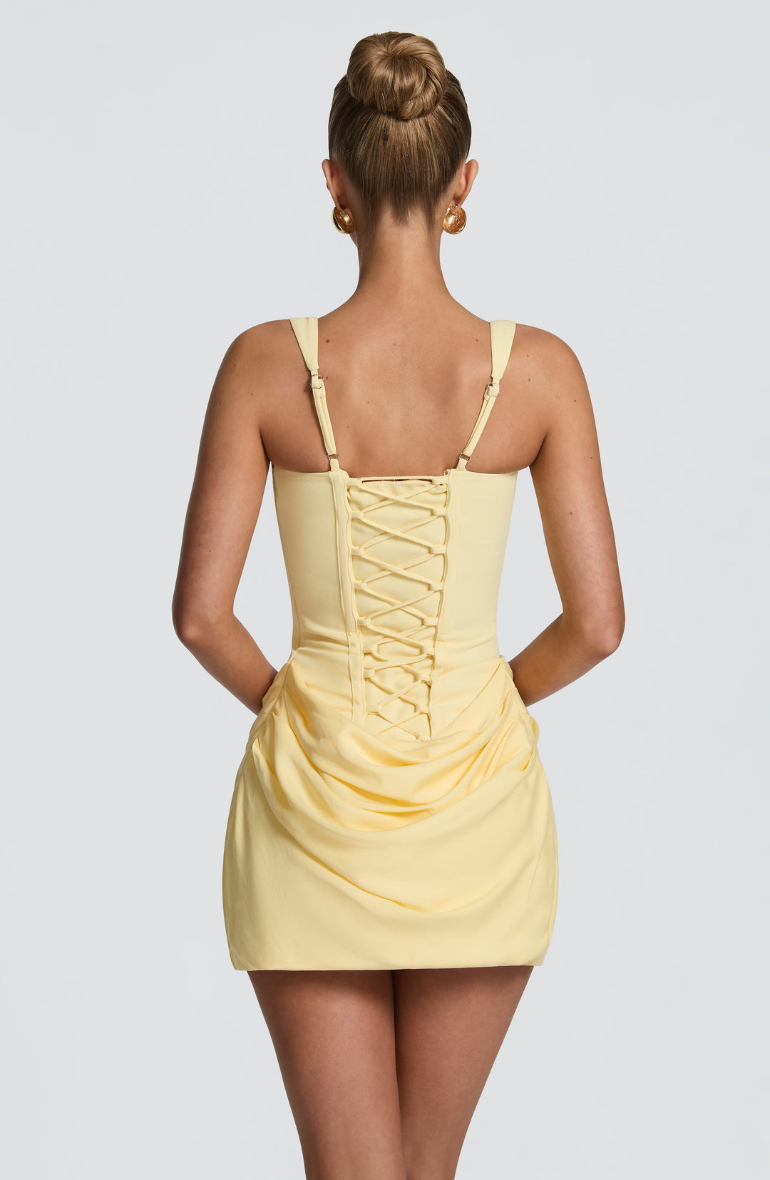Dos de la robe jaune pâle avec laçage croisé façon corset, bretelles réglables et jupe drapée à ourlet arrondi. 26