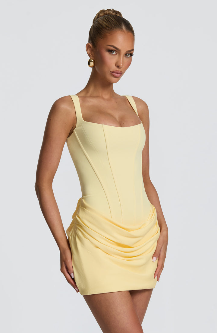 Robe jaune pâle vue de trois quarts, avec encolure carrée, buste corseté à coutures apparentes et jupe drapée. 27
