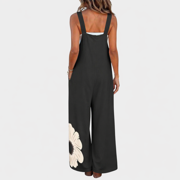 Salopette noire vue de dos sur un modèle, larges bretelles et fleur crème en bas de la jambe 3