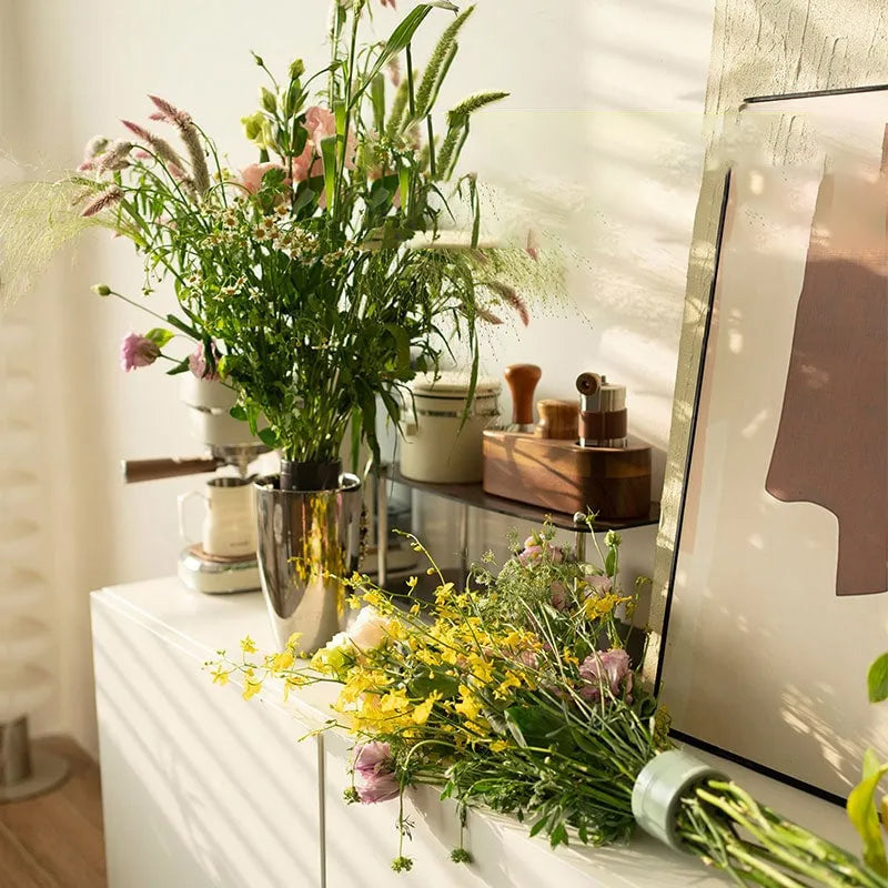 Bouquets de fleurs sauvages dans un vase en métal sur un meuble blanc, un autre bouquet posé à côté, lié par un insert vert. 3