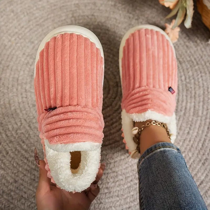 Chaussons roses côtelés vus de dessus, l'un tenu en main et l'autre porté, sur un tapis gris. 10