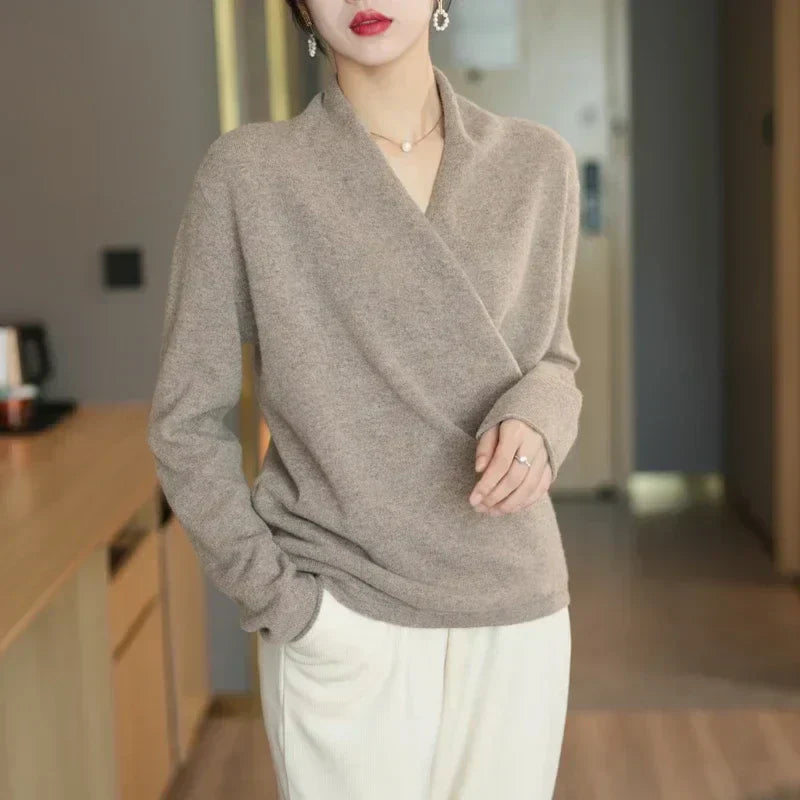 Pull croisé beige taupe porté debout avec un pantalon blanc cassé, une main dans la poche 7
