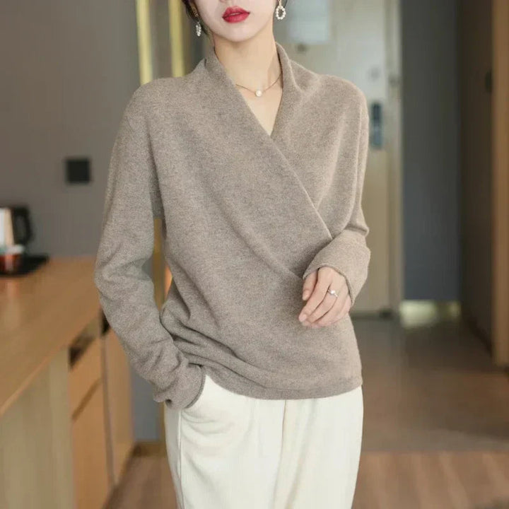 Pull croisé beige taupe porté debout avec un pantalon blanc cassé, une main dans la poche 7