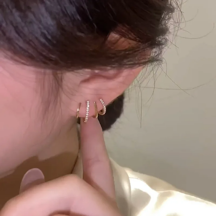 Boucle à quatre griffes fines dorées portée à l'oreille, un doigt pointé vers le bijou 3