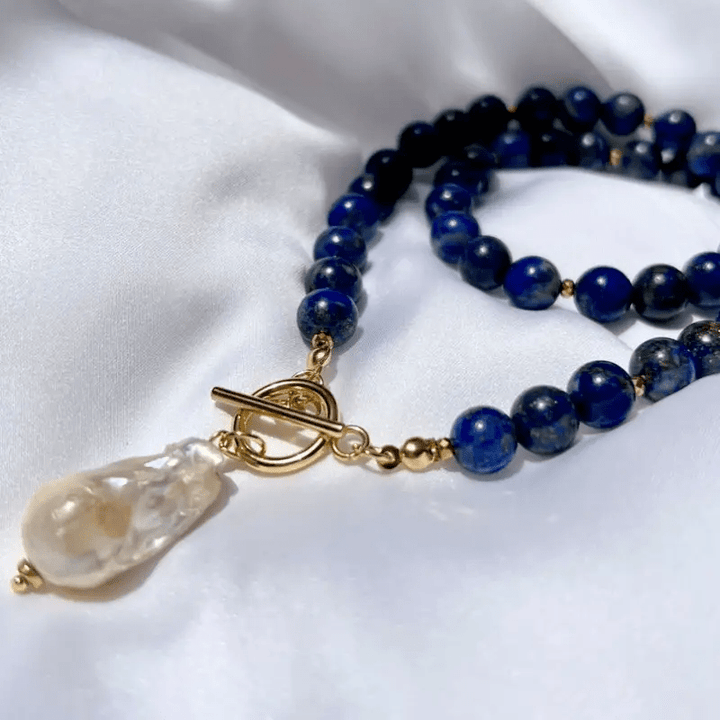 Gros plan sur le fermoir doré et la perle baroque, collier posé sur un tissu blanc 5