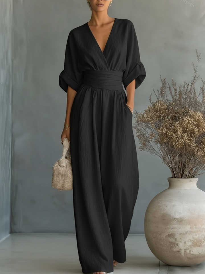 Combinaison noire portée de face, col en V, ceinture plissée et jambes larges, sac tressé à la main 4