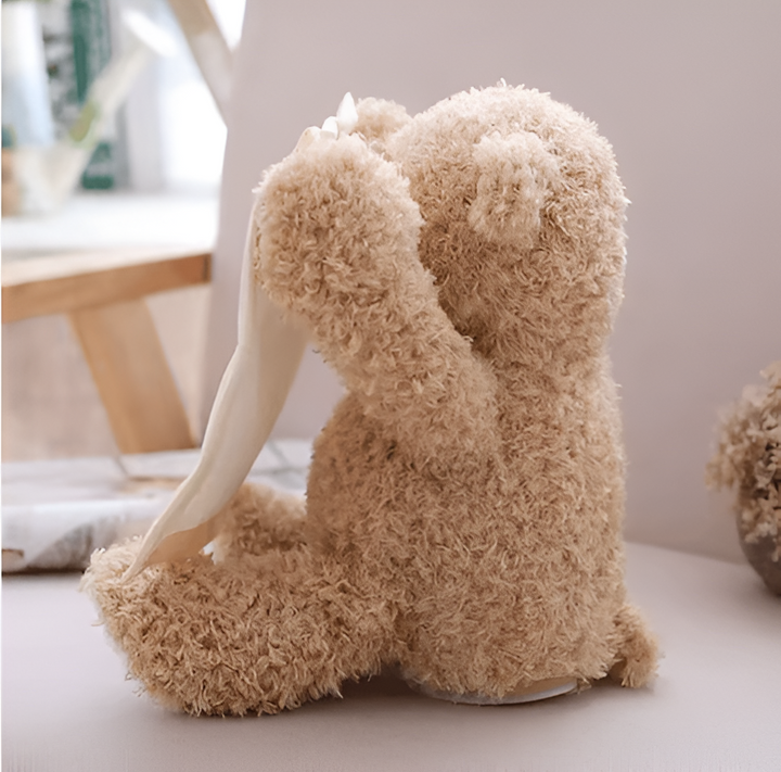 Ours en peluche vu de profil et de dos, un bras replié devant le visage, le tissu crème pendant sur le côté. 3
