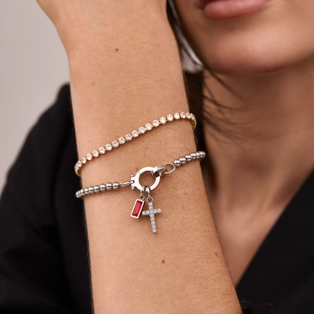 Version argentée du bracelet à perles avec croix et pierre rouge, portée en duo avec un bracelet doré serti de strass. 4
