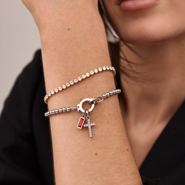Version argentée du bracelet à perles avec croix et pierre rouge, portée en duo avec un bracelet doré serti de strass. 4