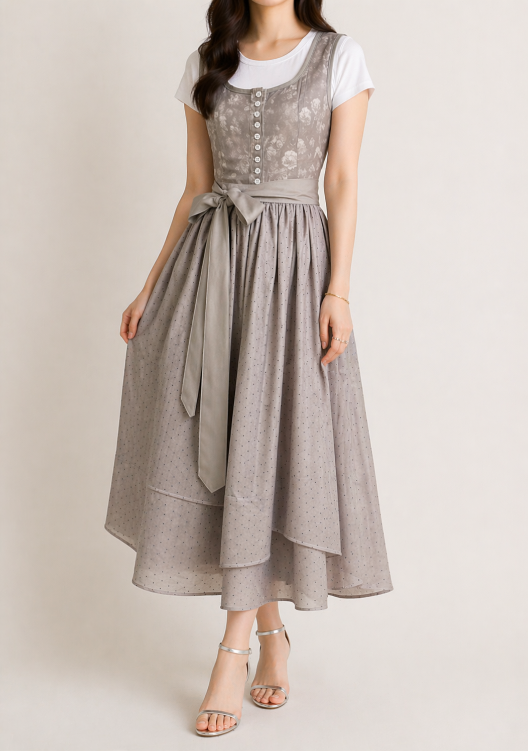 Robe dirndl grise portée par une mannequin, vue de face en pied, avec jupe ample à pois, ceinture nouée et sandales argentées. 2