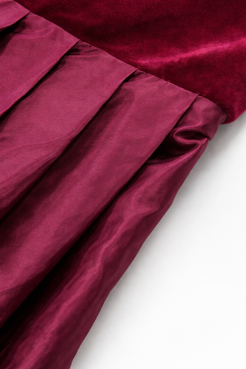 Gros plan sur la couture de taille entre le velours du corsage et la jupe plissée à l'aspect satiné. 2