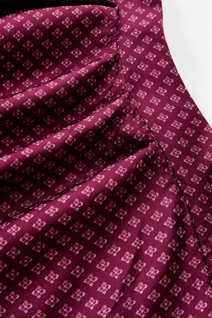 Détail du tissu du tablier, petits motifs de fleurs sur fond bordeaux, avec plis et couture visibles. 3