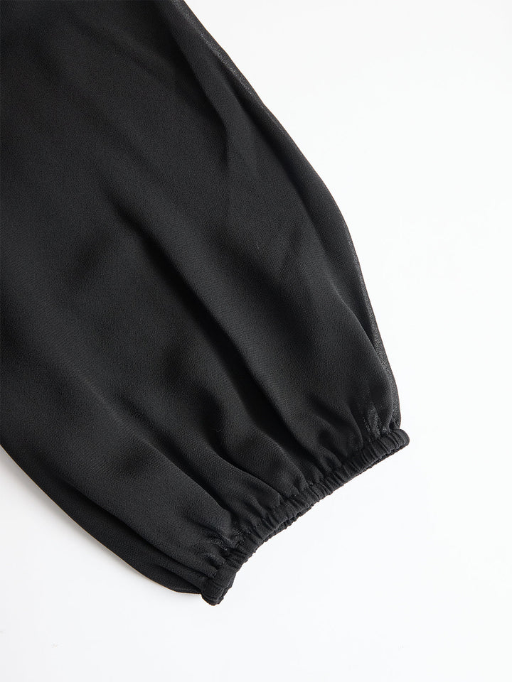 Gros plan sur une manche bouffante transparente noire à poignet élastiqué, posée à plat sur fond blanc. 4