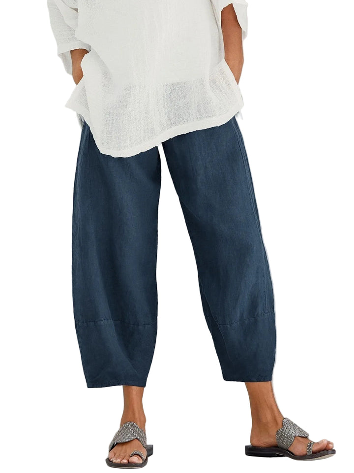 Pantalon large bleu marine à taille élastique, porté avec une blouse blanche légère et des sandales, mains dans les poches. 1