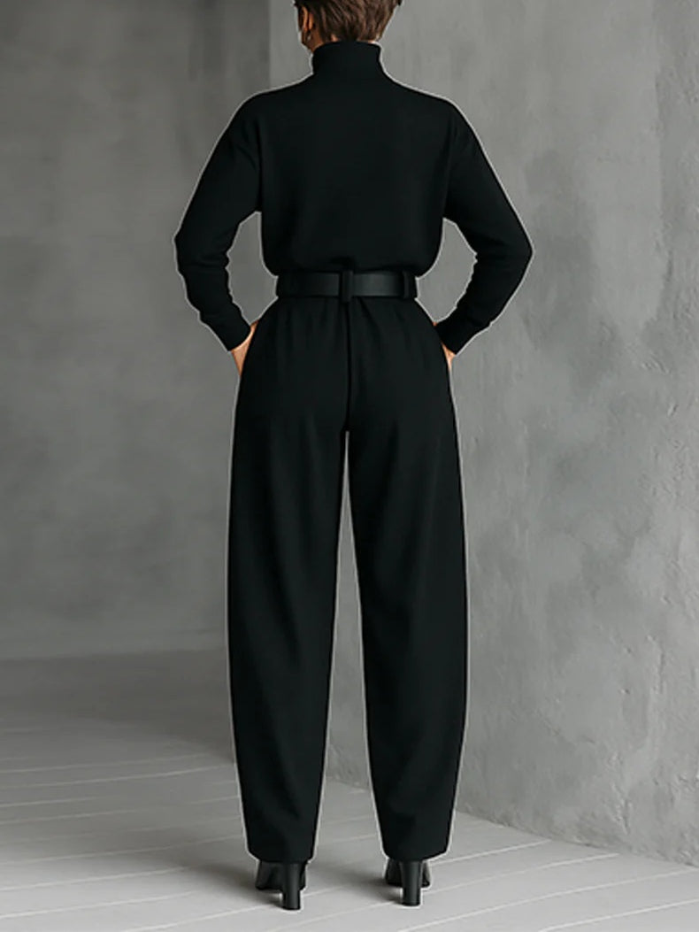 Vue de dos de l'ensemble noir porté avec ceinture et bottines, devant un mur gris 2
