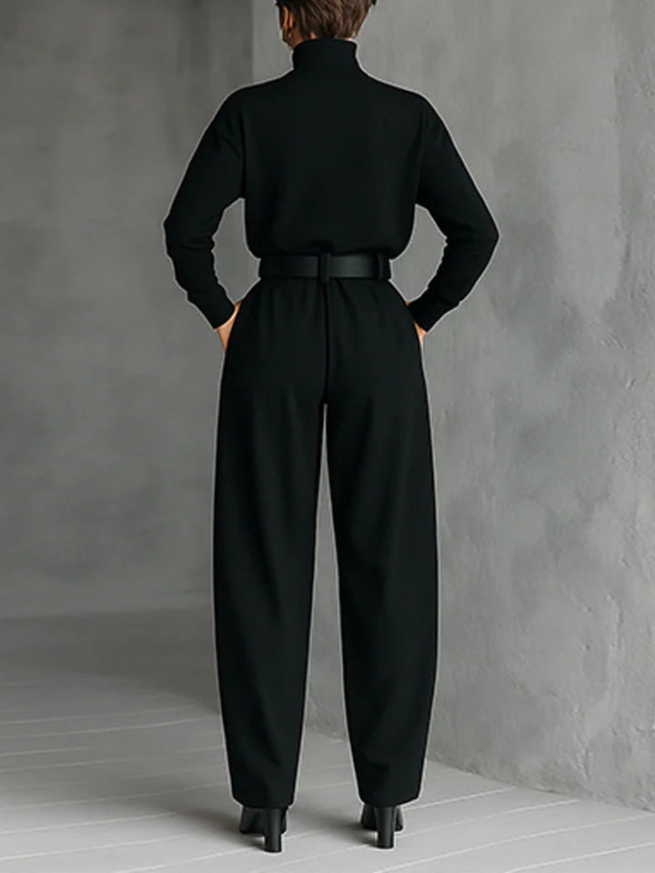 Vue de dos de l'ensemble noir porté avec ceinture et bottines, devant un mur gris 2