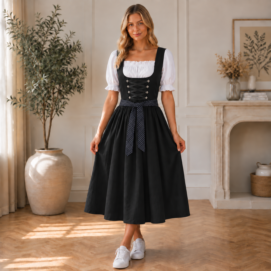 Femme debout en robe midi noire, blouse blanche et baskets blanches, dans un salon clair avec cheminée et olivier. 2