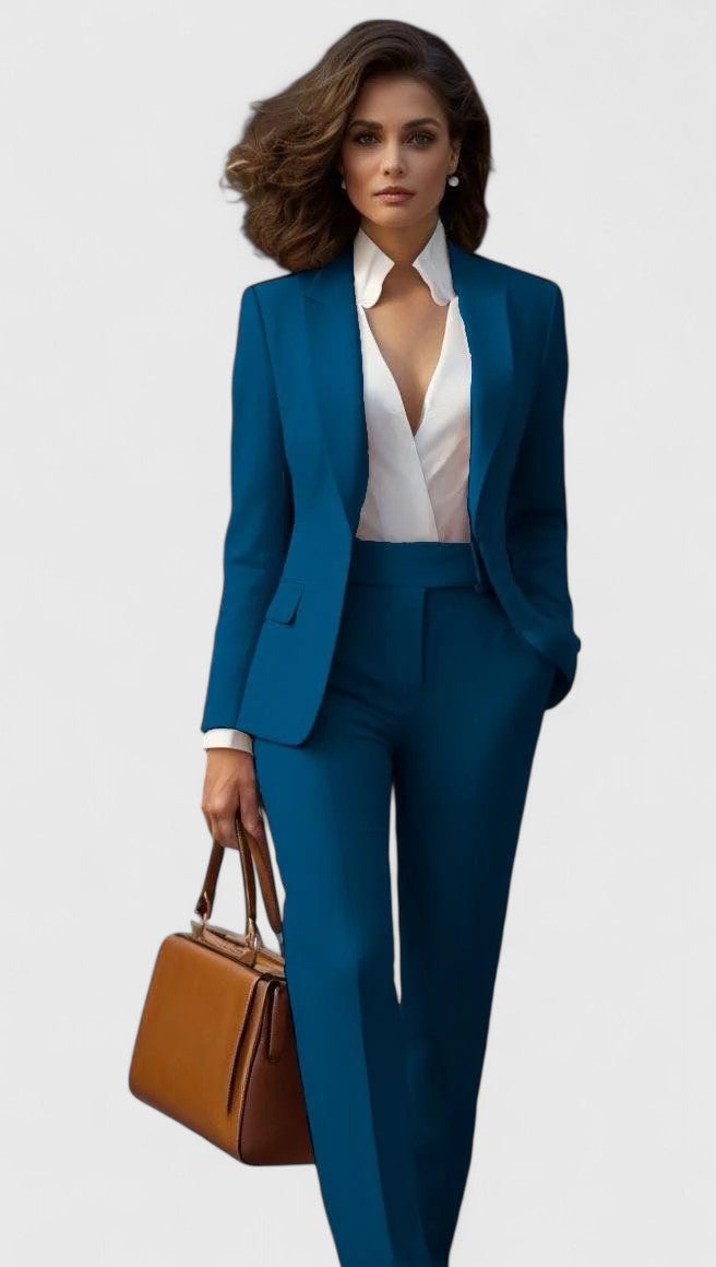 Femme en ensemble bleu pétrole, blazer ouvert sur un chemisier blanc, pantalon taille haute, sac en cuir marron à la main. 2