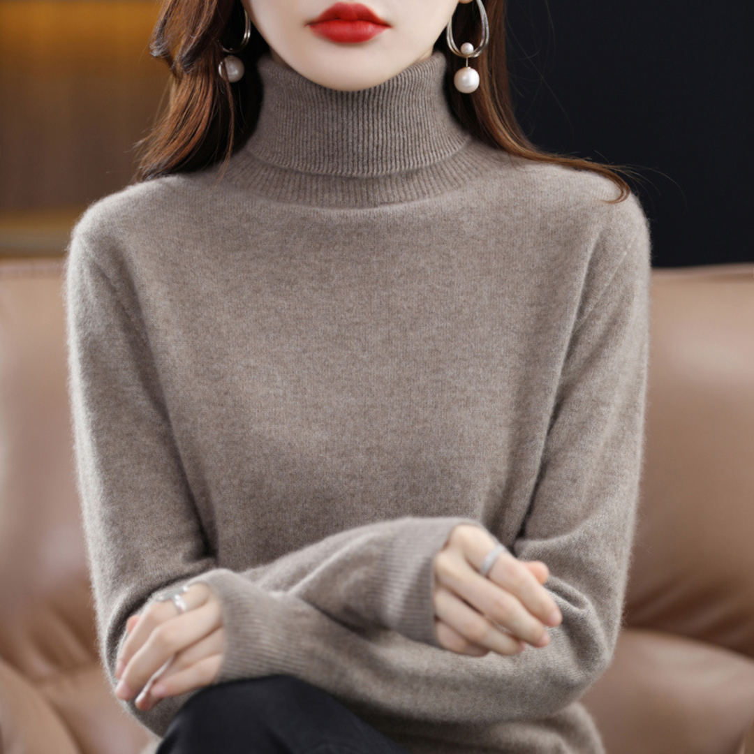 Pull taupe à col roulé porté par une femme assise sur un canapé en cuir, mains jointes. 13