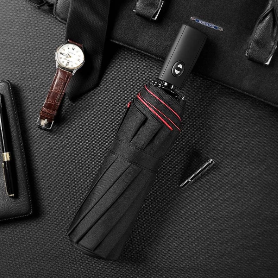 Parapluie noir replié, liseré rouge, posé sur un sac avec montre, cravate et stylos 1