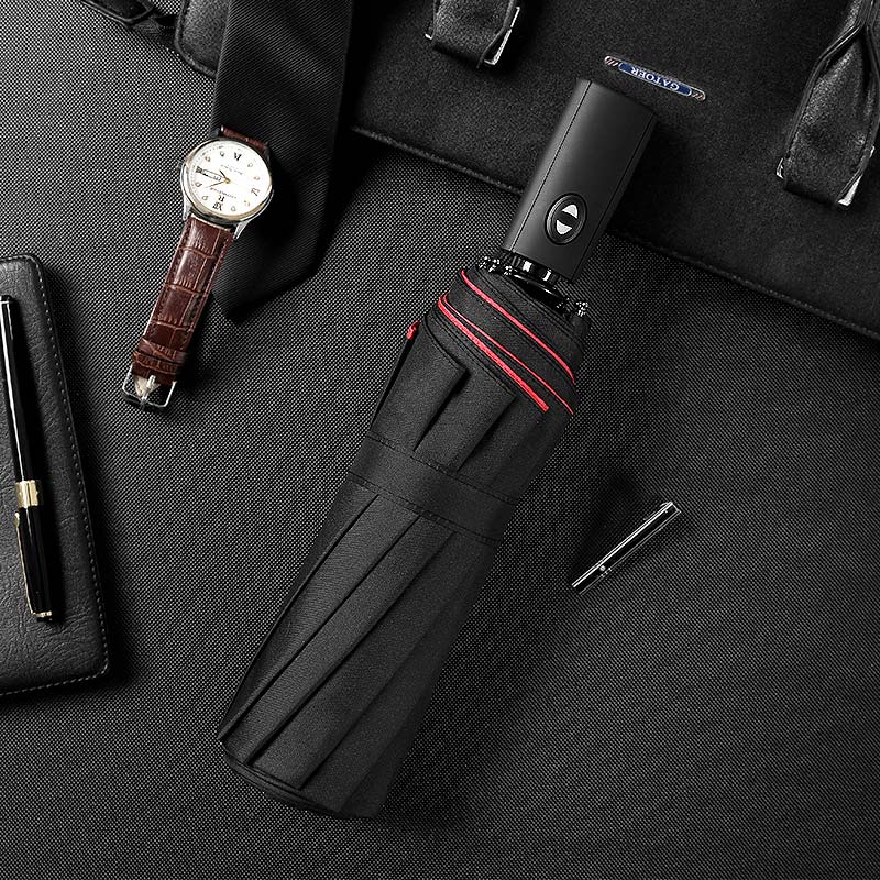 Parapluie noir replié à liseré rouge posé sur un sac, avec montre en cuir et stylos 11