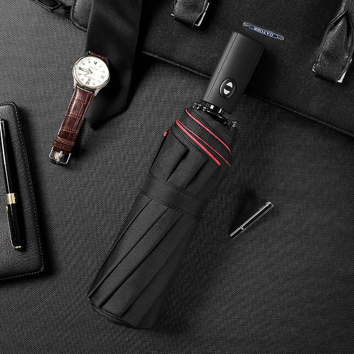 Parapluie noir replié à liseré rouge posé sur un sac, avec montre en cuir et stylos 11