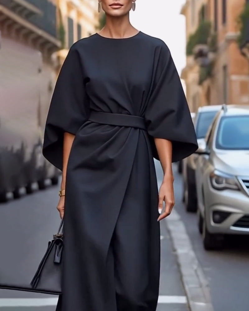 Robe noire ceinturée à manches amples, portée en plan rapproché avec des boucles d'oreilles et un sac noir dans une rue bordée de voitures. 4