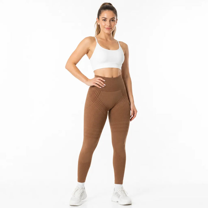 Femme de face en legging marron caramel taille haute avec lignes texturées sur les hanches, brassière blanche, baskets blanches. 17