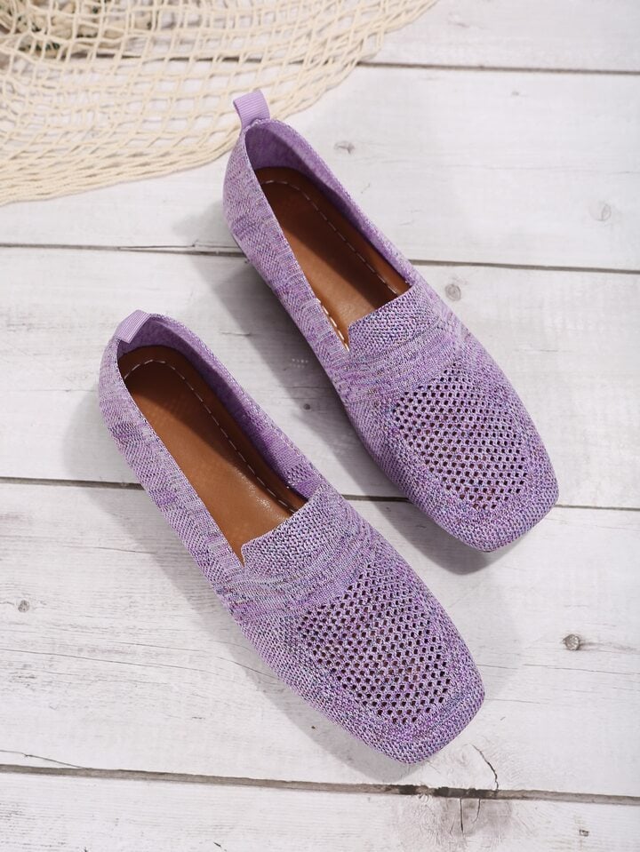 Paire violette en maille posée à plat sur un plancher blanc, intérieur marron cousu et languette de talon visibles. 13