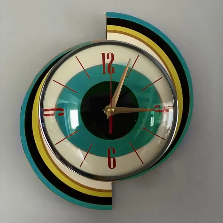 Vue de face de l'horloge spirale, cadran turquoise et noir à chiffres rouges, encadré de bandes turquoise, jaune et noires. 11